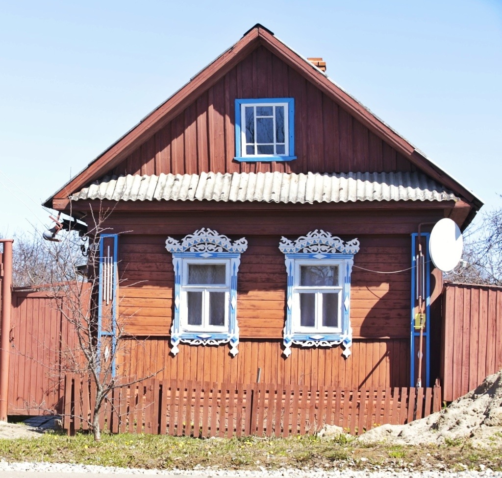 A brown wooden house with blue nalichniki (ornate wooden windows frames) |  Nalichniki.com